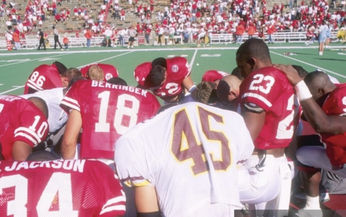 Nebraska football players gathered in a huddle around a Brook Berringer tribute jersey